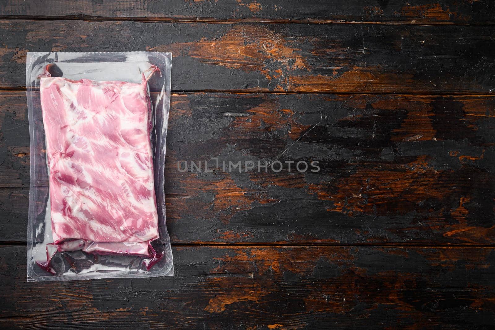Pork ribs in a vacuum bag set, on old dark wooden table background, top view flat lay, with copy space for text