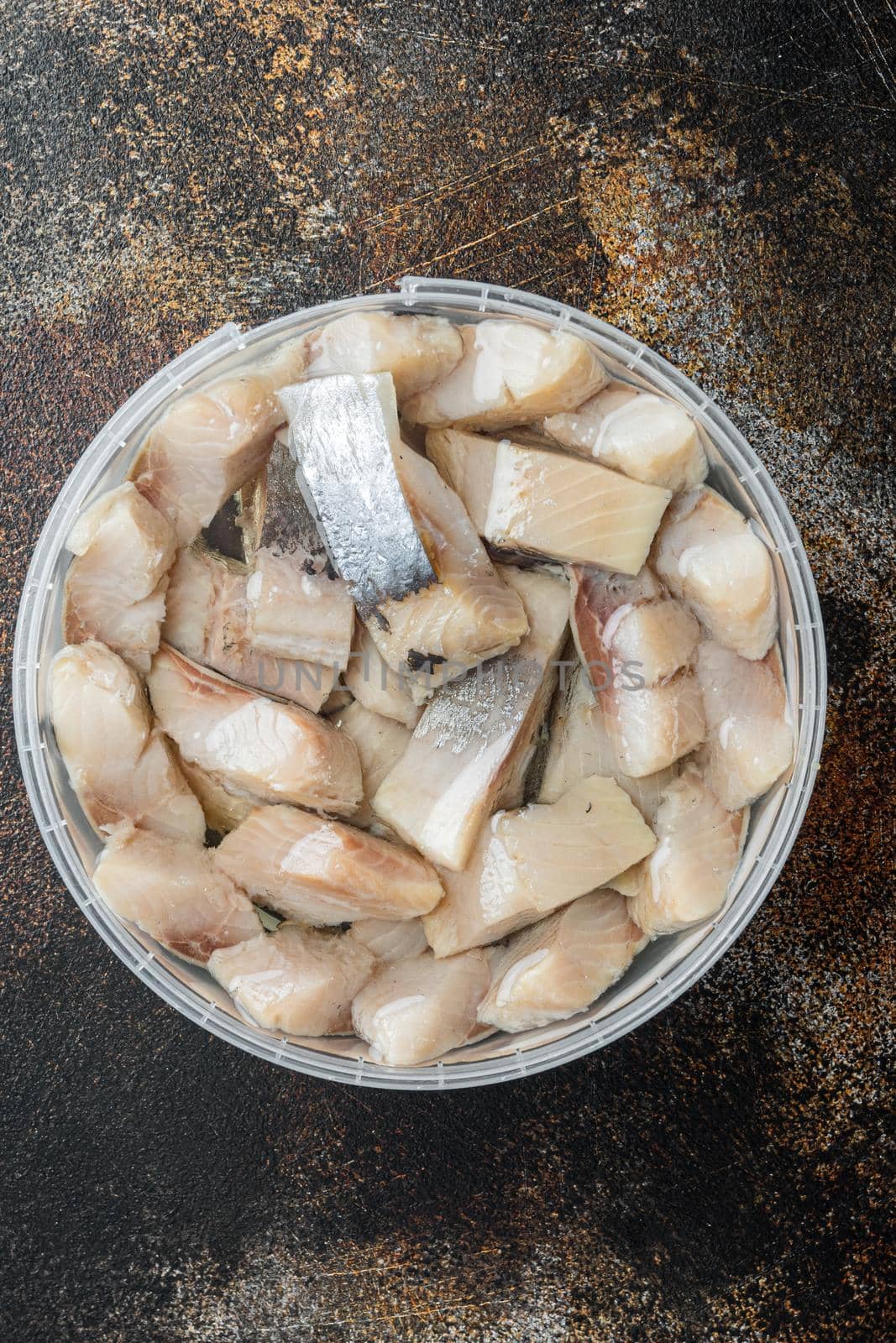Herring pieces drenched in oil, on old dark rustic background, top view flat lay