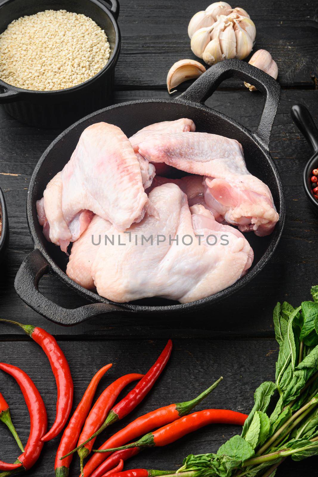 Raw chicken wings with herbs, and sesame, in frying cast iron pan, on black wooden table by Ilianesolenyi