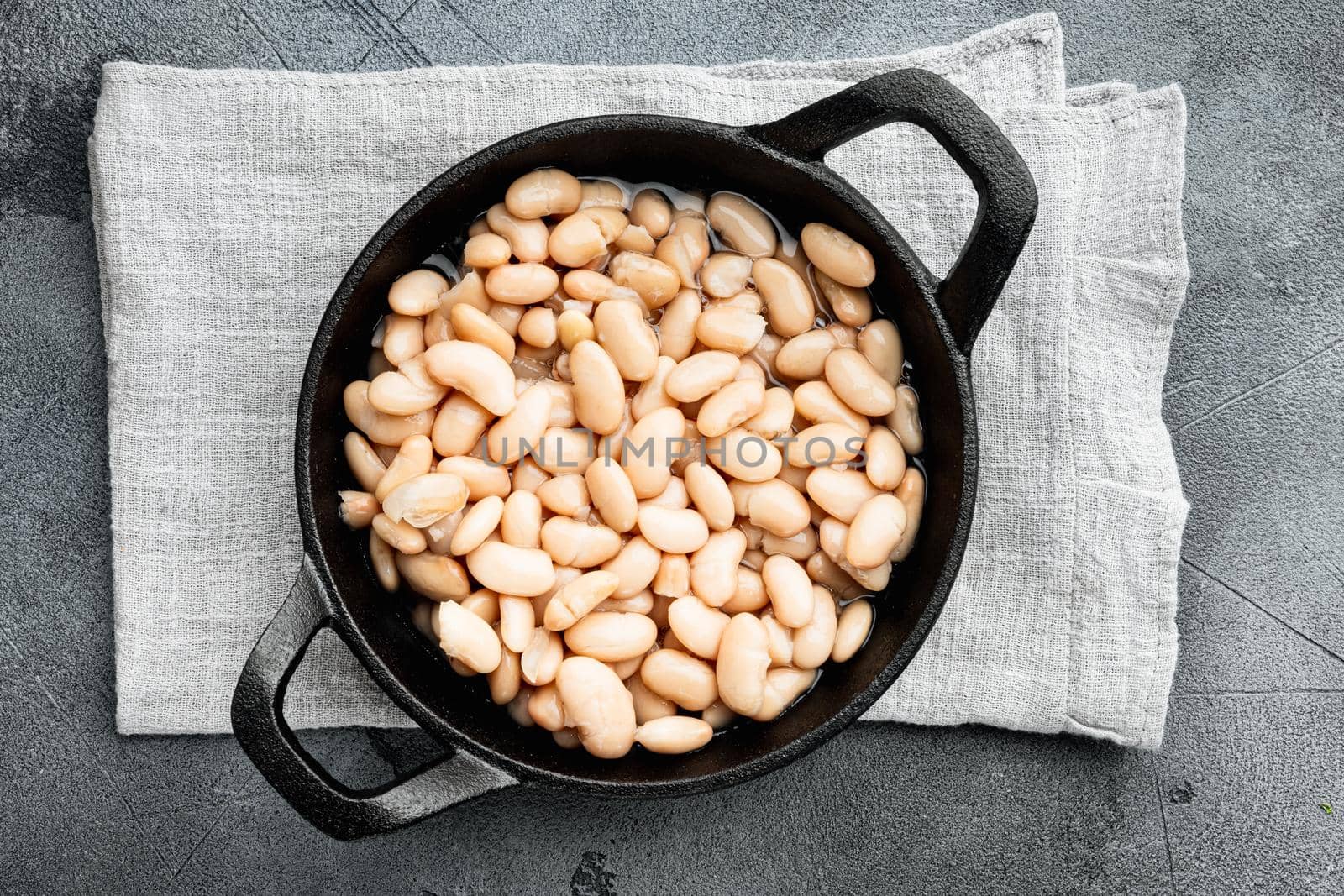White canned beans, in cast iron frying pan, on gray stone background, top view flat lay by Ilianesolenyi