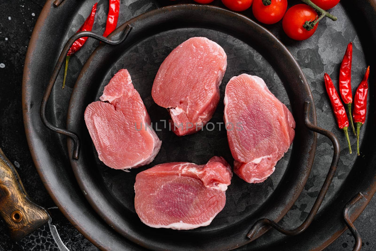 Pieces of raw pork steak with spices and herbs rosemary, on black dark stone table background, top view flat lay