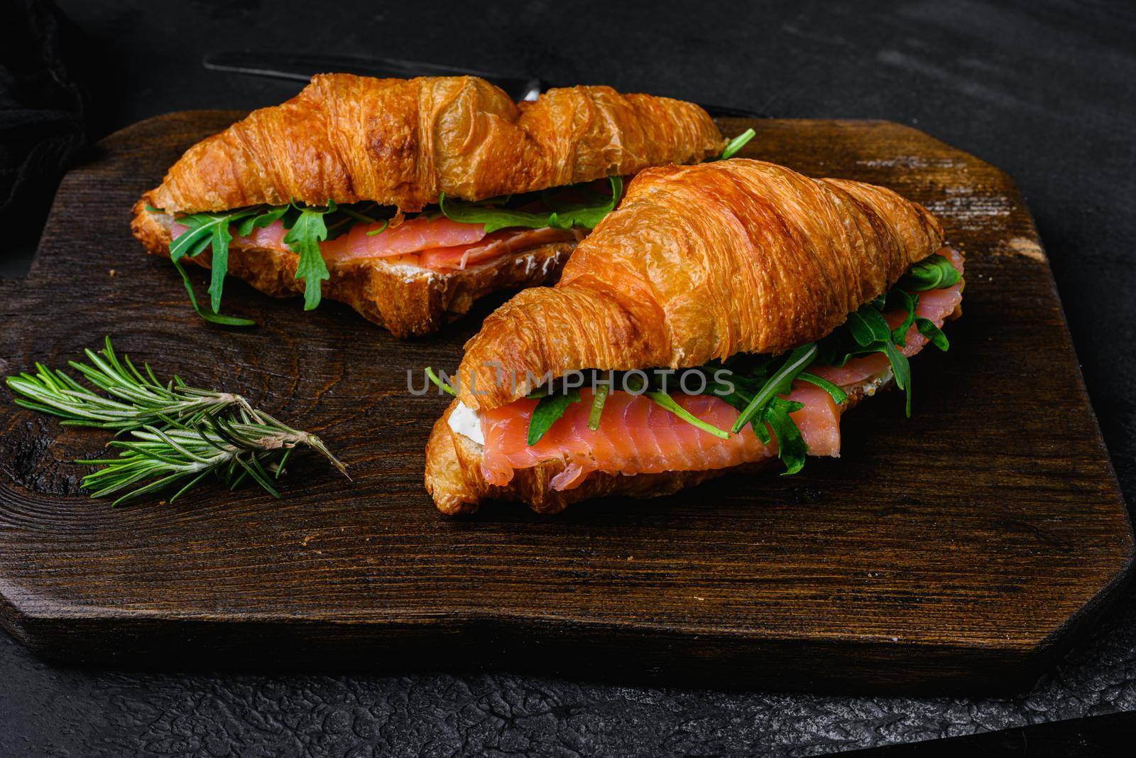 Croissant sandwich with salmon, on black dark stone table background by Ilianesolenyi