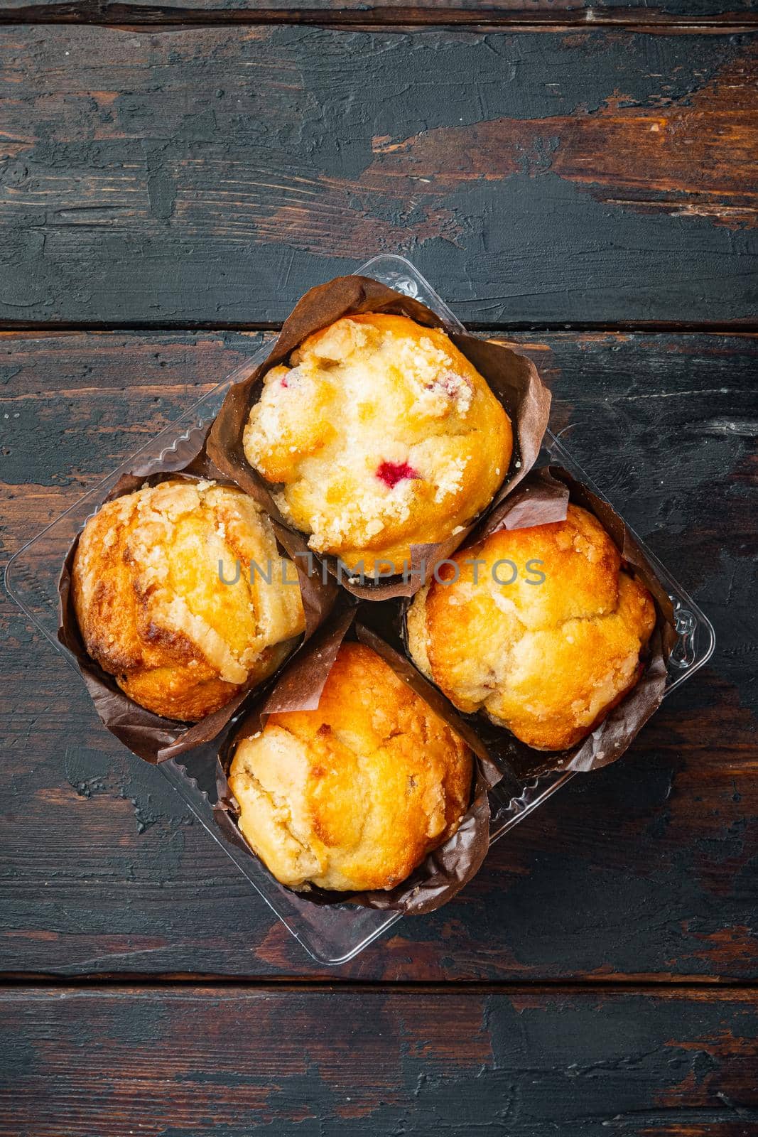 Muffins in plastic container box, on old dark wooden table background, top view flat lay by Ilianesolenyi