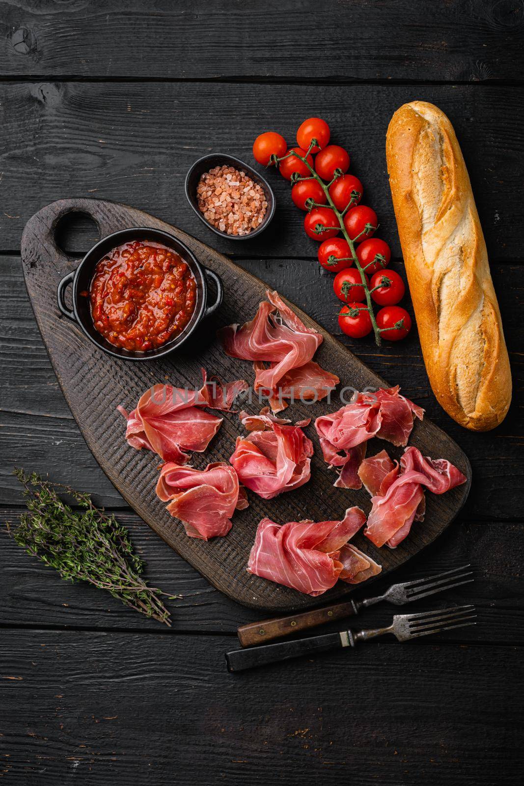 Italian prosciutto crudo or spanish jamon, on black wooden background, top view flat lay