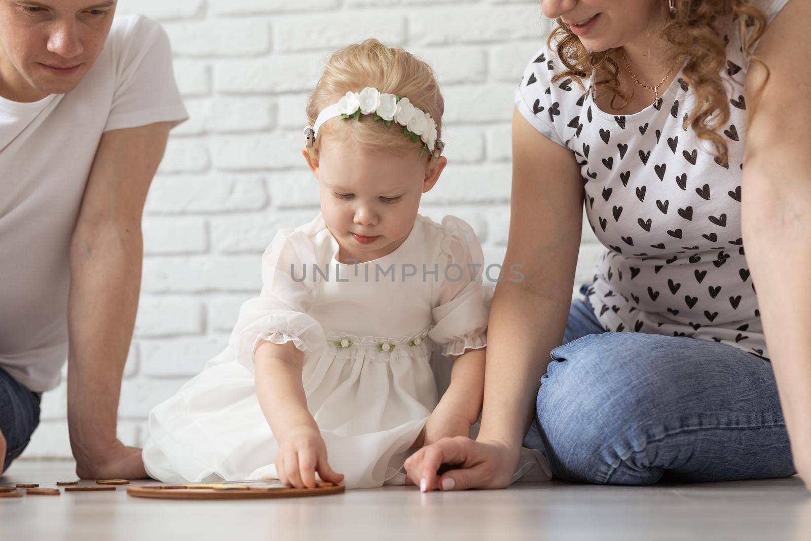 Baby child with hearing aids and cochlear implants plays with parents on floor. Deaf and rehabilitation and diversity concept by Satura86