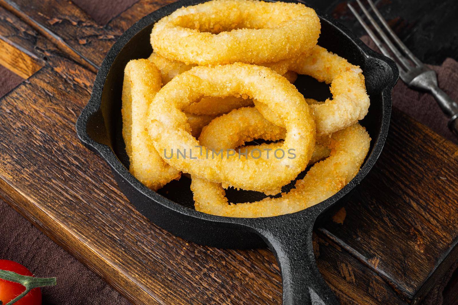 Squid rings or onion in breadcrumbs ingredients on cast iron frying pan skillet, on old dark wooden table background by Ilianesolenyi