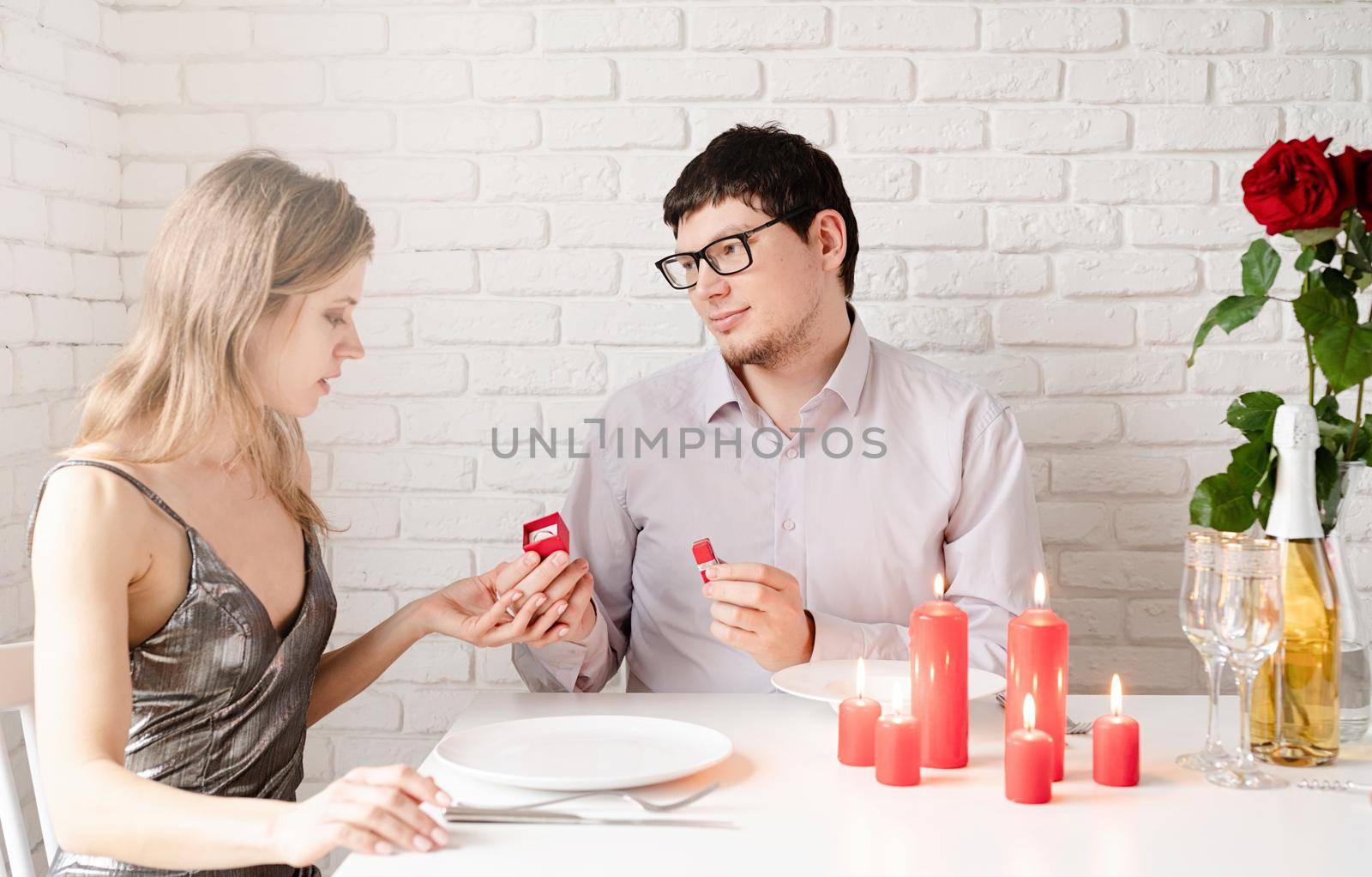 handsome man putting wedding ring on and proposing to his beautiful woman in cafe by Desperada