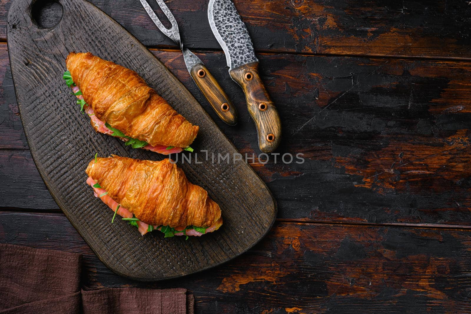 Croissant sandwich with salted salmon, on old dark wooden table background, top view flat lay, with copy space for text by Ilianesolenyi