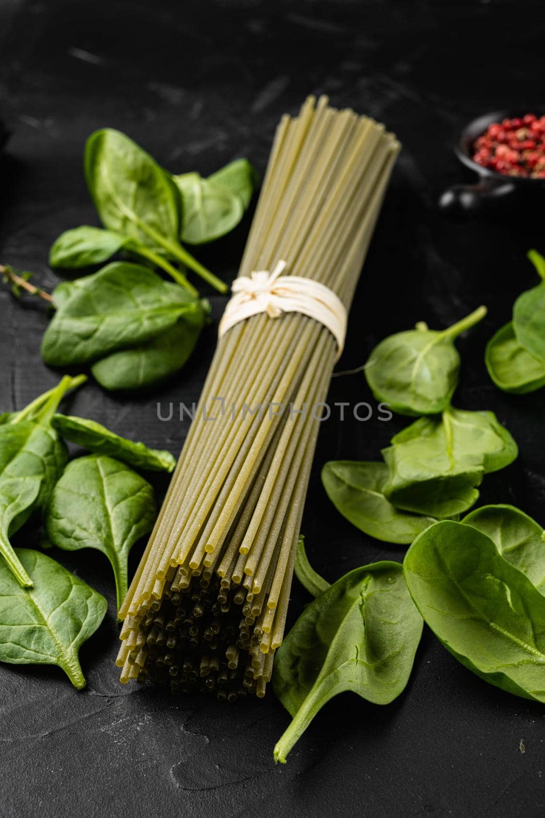 Raw dry green spaghetti with spinach set, on black dark stone table background