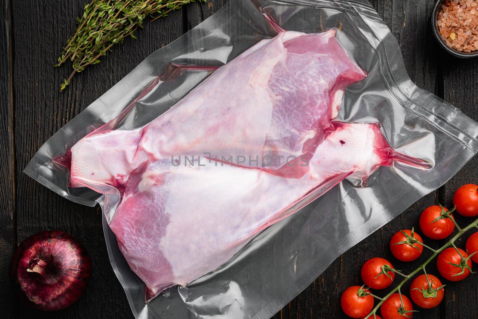 Raw turkey drumsticks and ingredients vacuum pack, top view flat lay, on black wooden table background by Ilianesolenyi