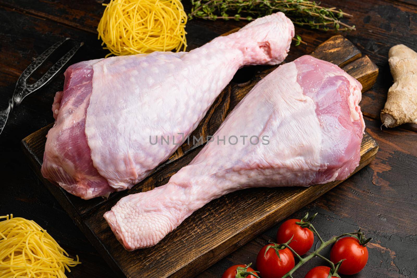 Fresh uncooked turkey legs set, on wooden cutting board, on old dark wooden table background