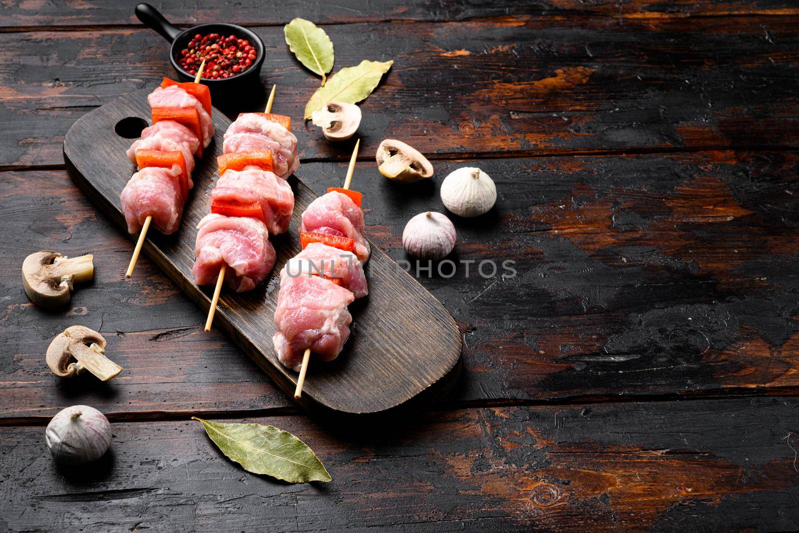 Kebabs raw meat and vegetables on skewers, with copy space for text, on old dark wooden table background by Ilianesolenyi