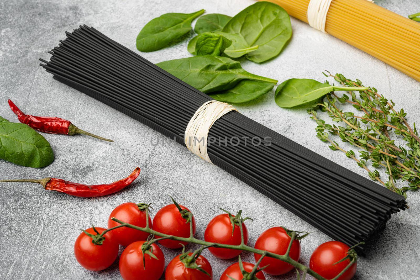 Squid ink black tinted twirl of raw tagliatelle, on gray stone table background by Ilianesolenyi