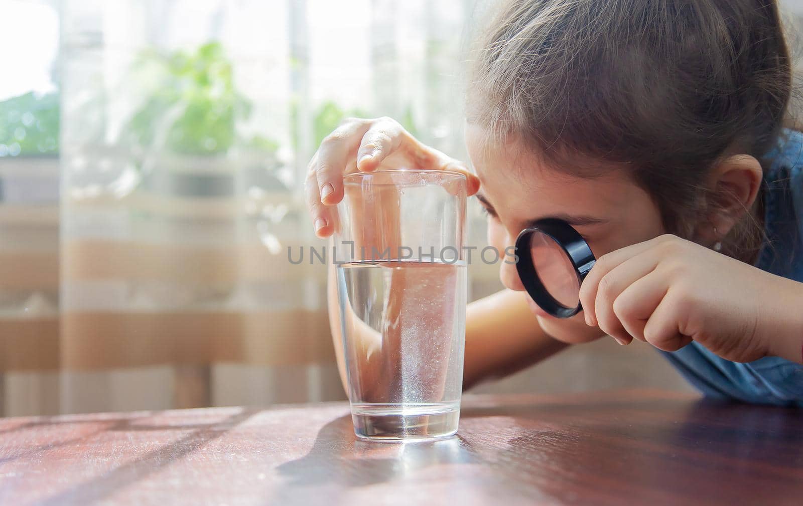 The child examines the water with a magnifying glass in a glass. Selective focus. by yanadjana