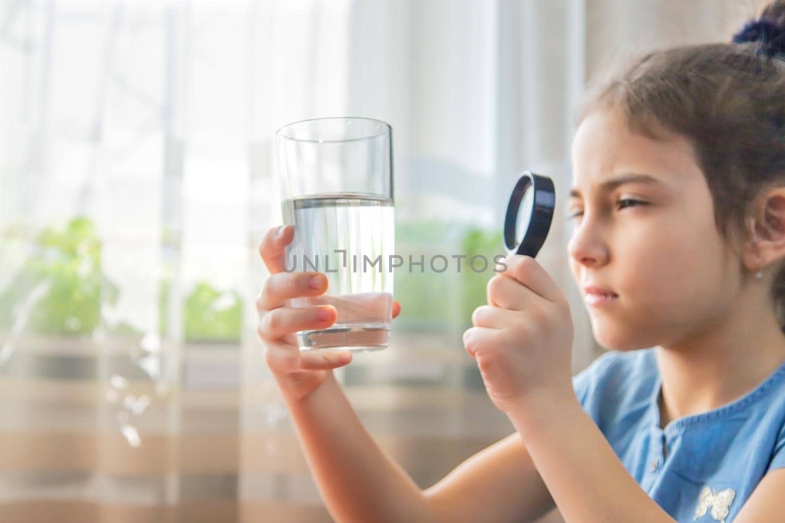 The child examines the water with a magnifying glass in a glass. Selective focus. by yanadjana