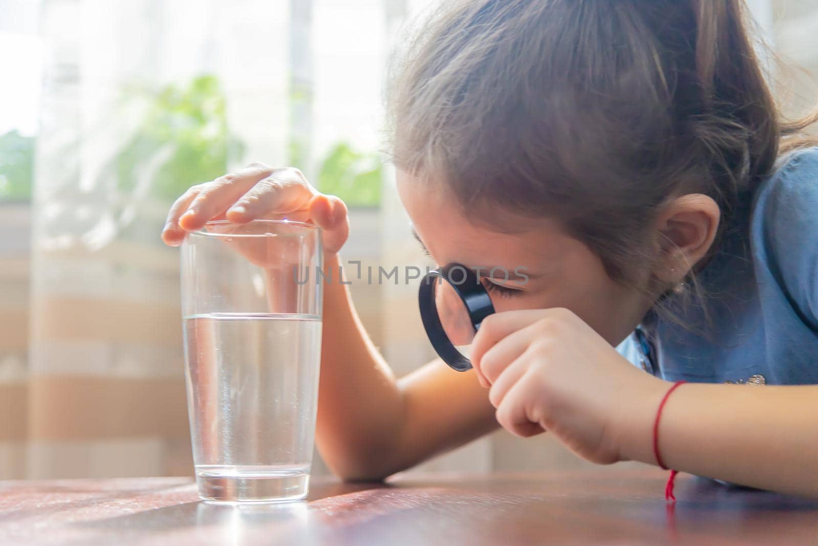 The child examines the water with a magnifying glass in a glass. Selective focus. by yanadjana
