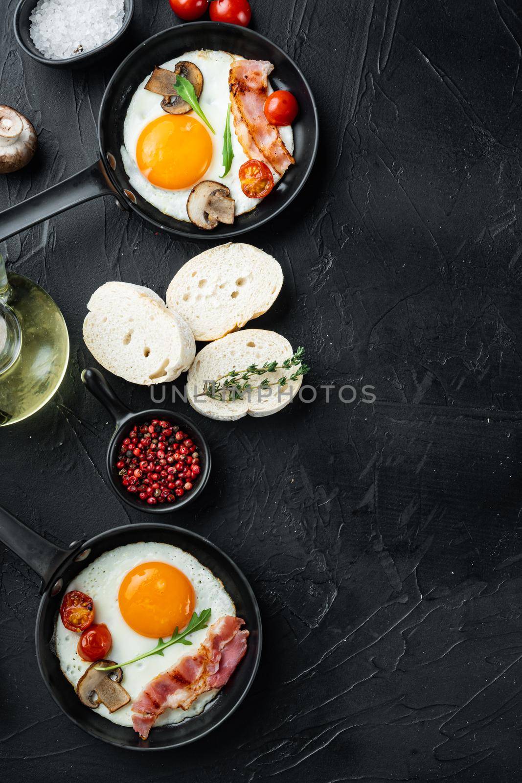 Scrambled eggs in frying pan with pork lard, bread and green feather in cast iron frying pan, on black background, top view flat lay , with space for text copyspace