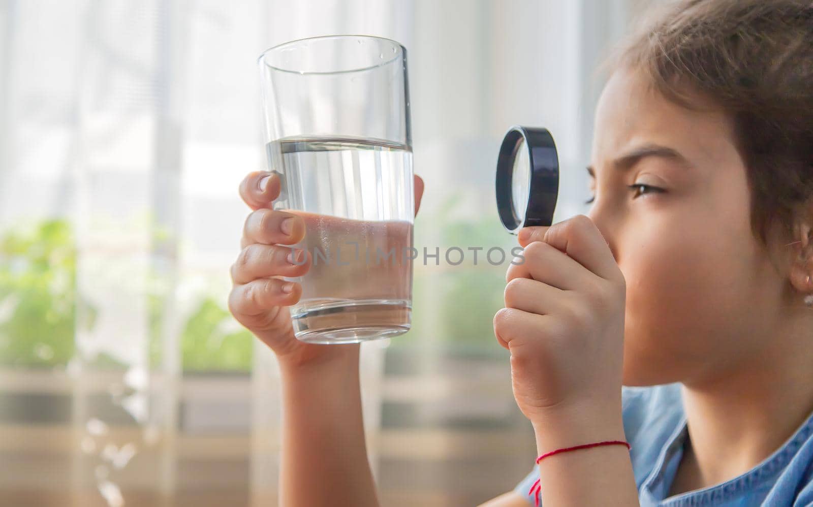 The child examines the water with a magnifying glass in a glass. Selective focus. Kid.