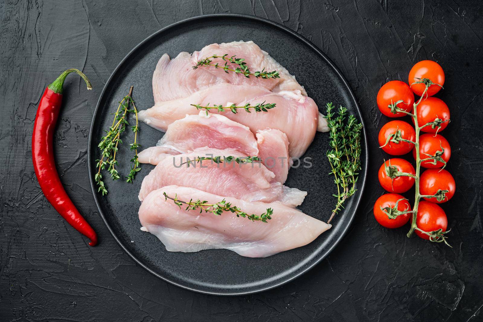 Pieces of raw and uncooked chicken fillet, on black background, top view flat lay by Ilianesolenyi