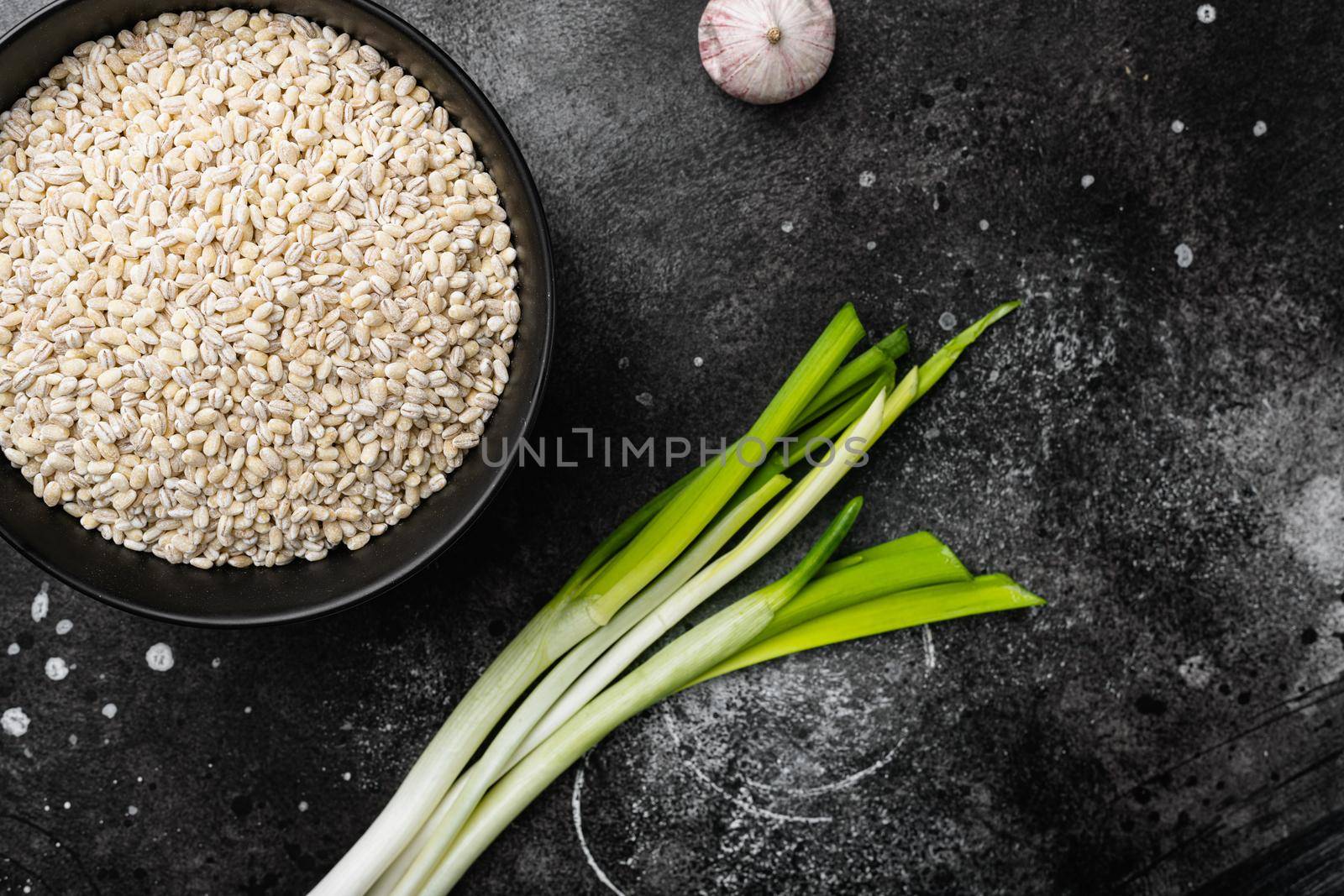 Raw pile of pearl barley set, on black dark stone table background, top view flat lay, with copy space for text