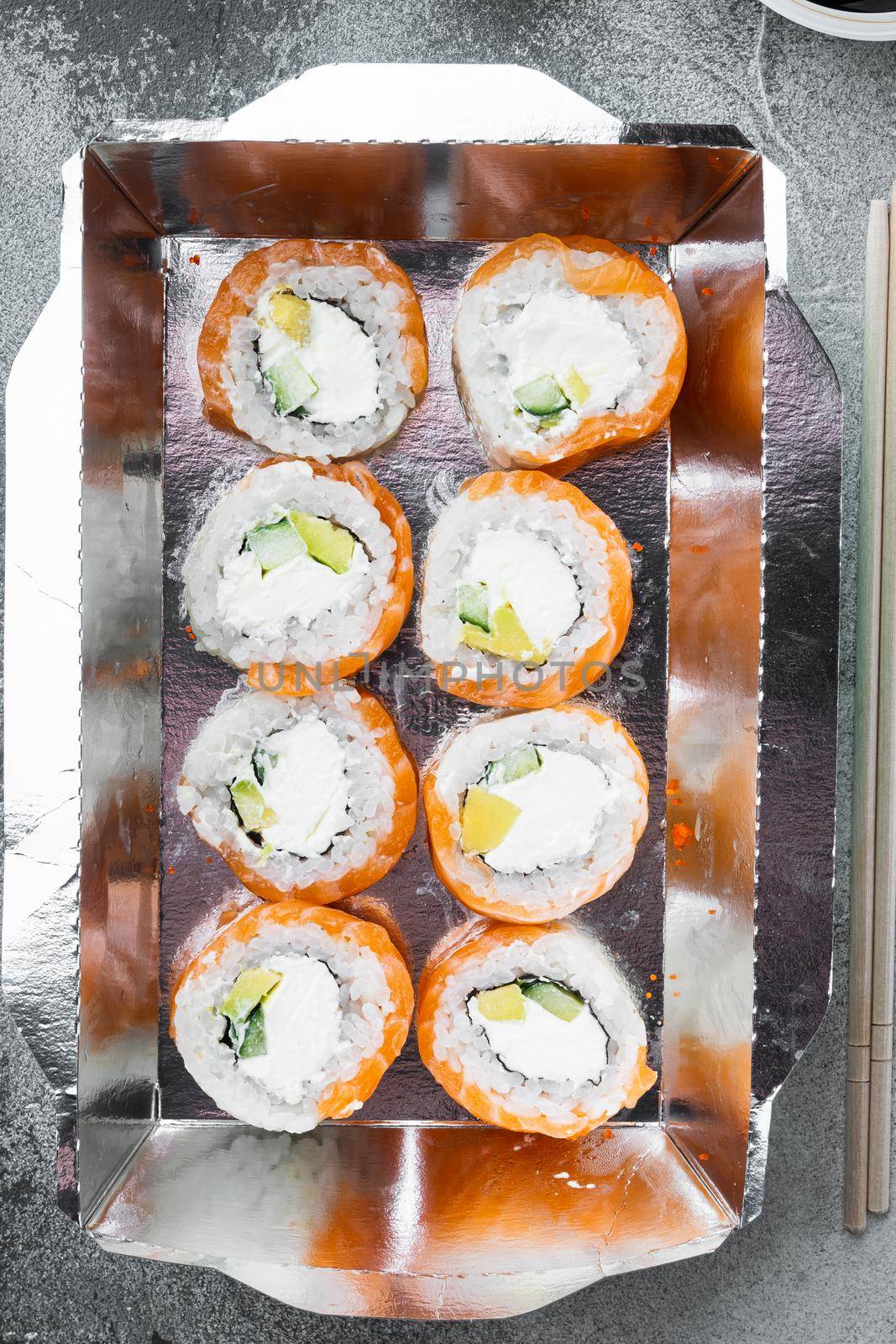 Sushi rolls in takeaway container set, on gray stone background, top view flat lay