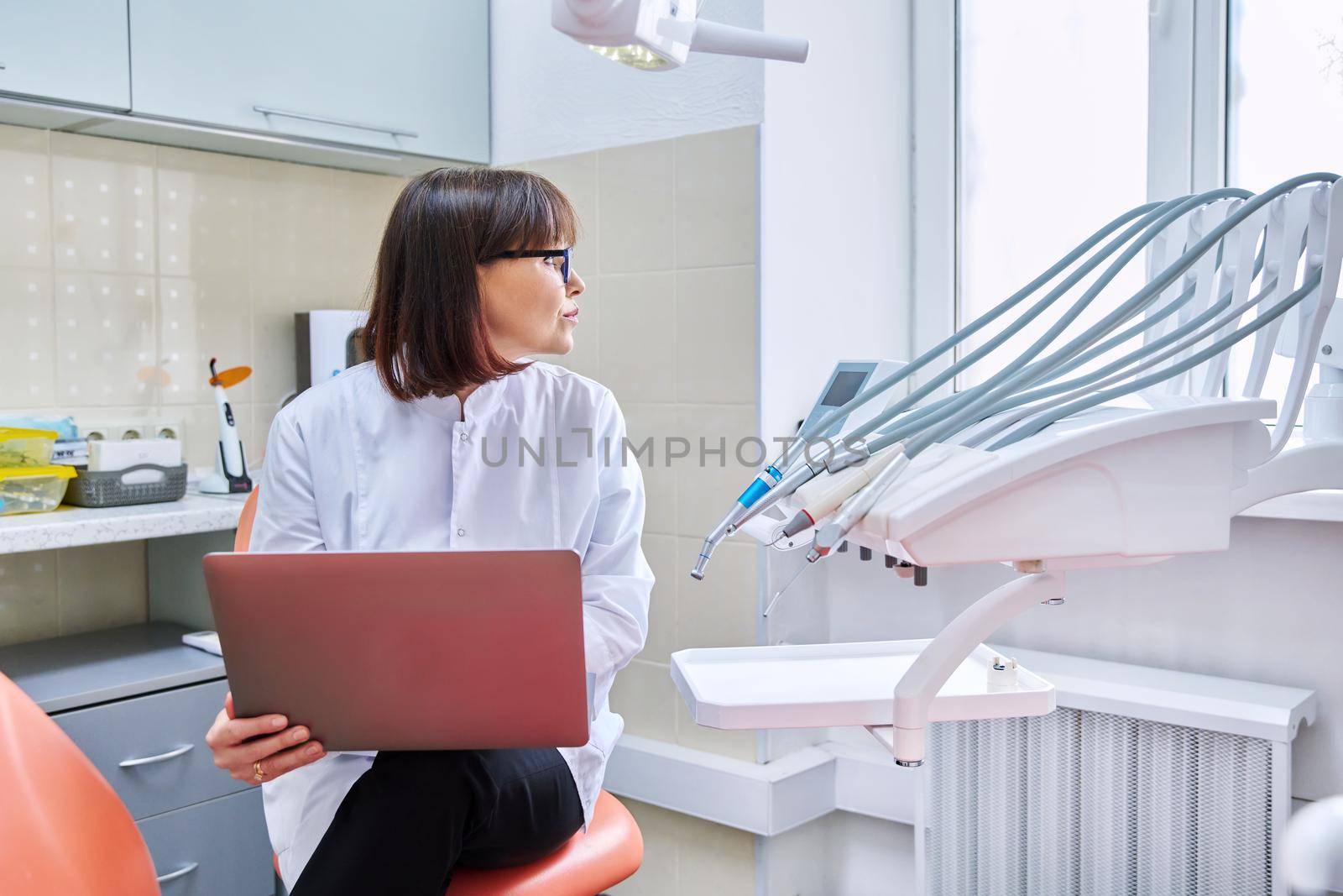 Doctor dentist sitting in the office using a laptop by VH-studio