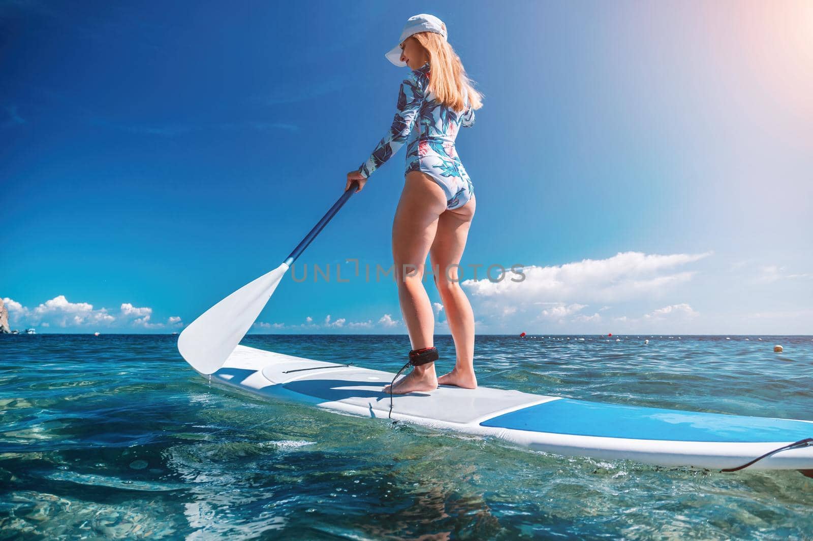 Healthy happy fit woman in bikini relaxing on a sup surfboard, floating on the clear turquoise sea water. Recreational Sports. Stand Up Paddle boarding. Summer fun, holidays travel. Active lifestyle by panophotograph