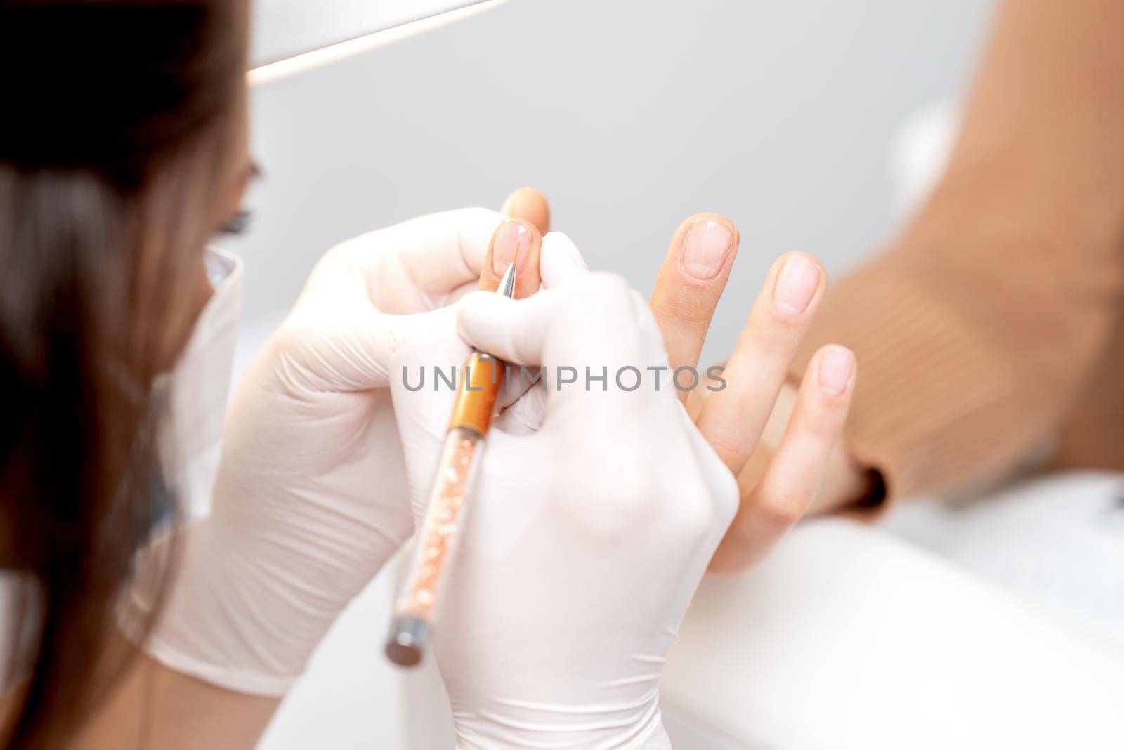 Professional manicure master drawing decorations by pink gel pencil on edge of a nail of young female