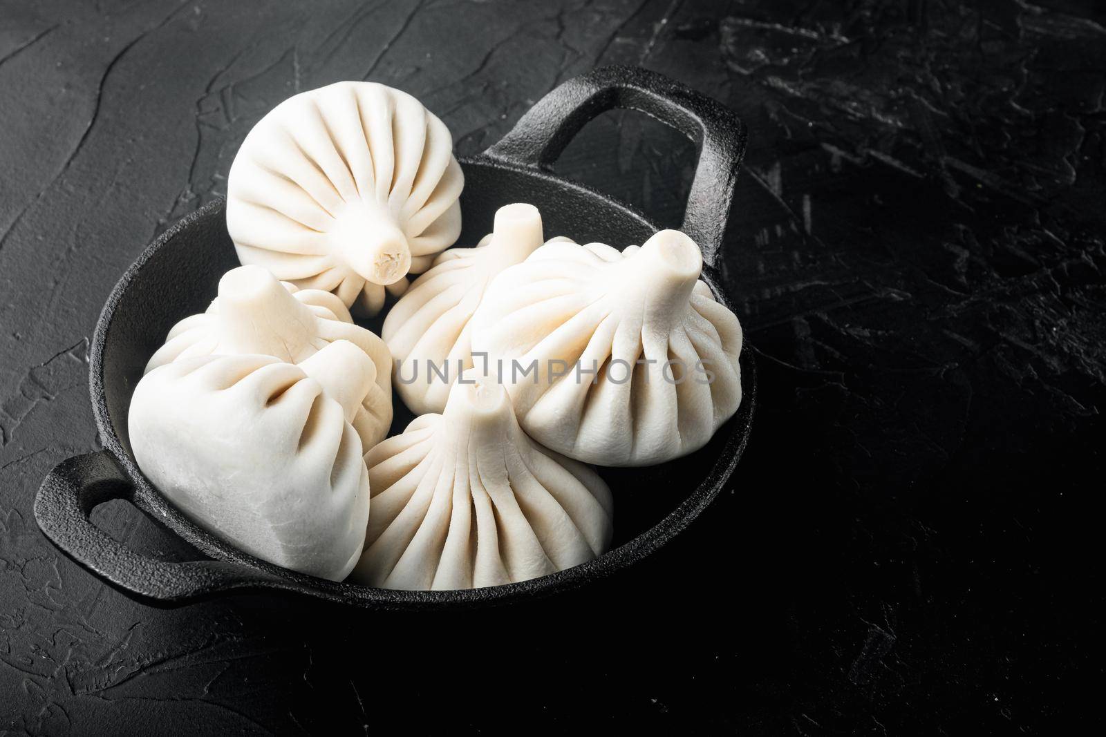 Frozen Raw dumplings Khinkali with beef and lamb meat set, in frying cast iron pan, on black stone background, with copy space for text