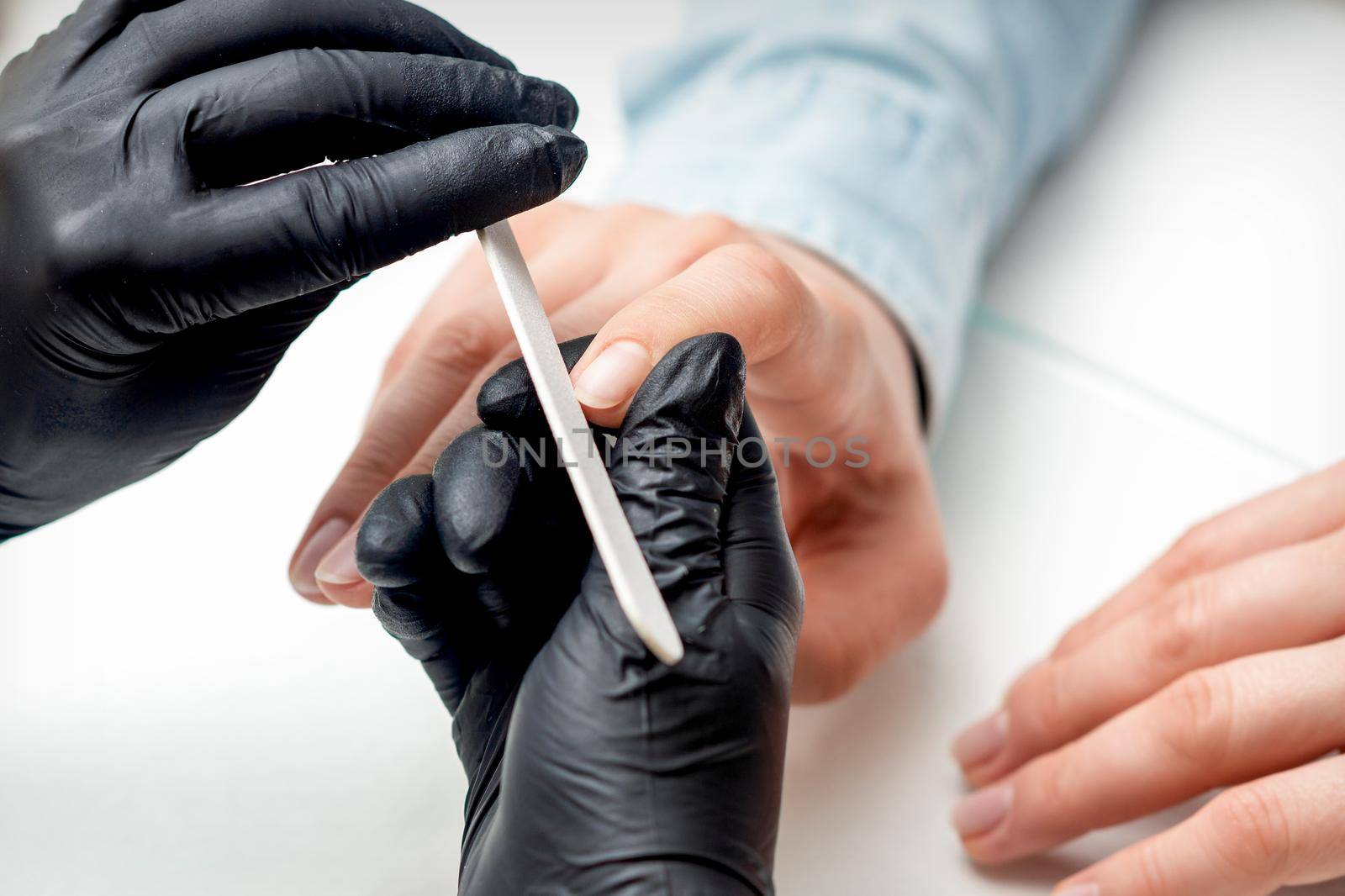 Closeup shot of young woman getting manicure by manicure master with nail file in nail salon