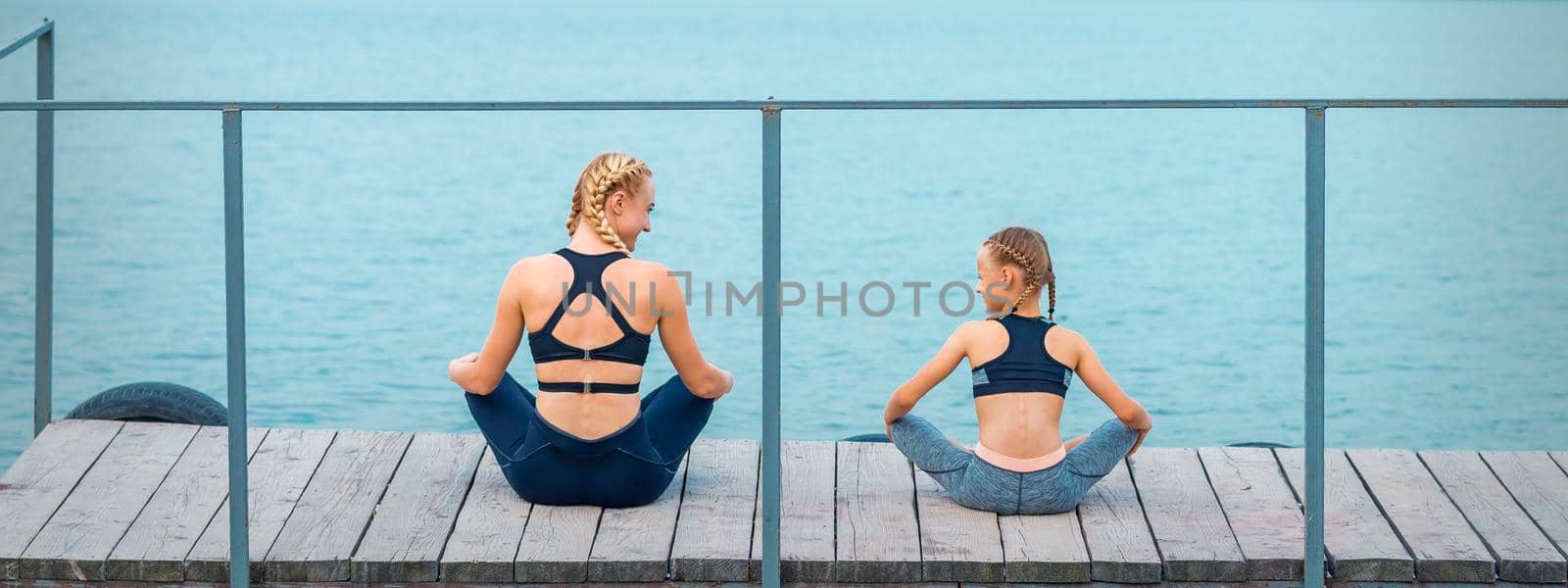 Mother and daughter doing gym exercises on the grass at the pier of the river