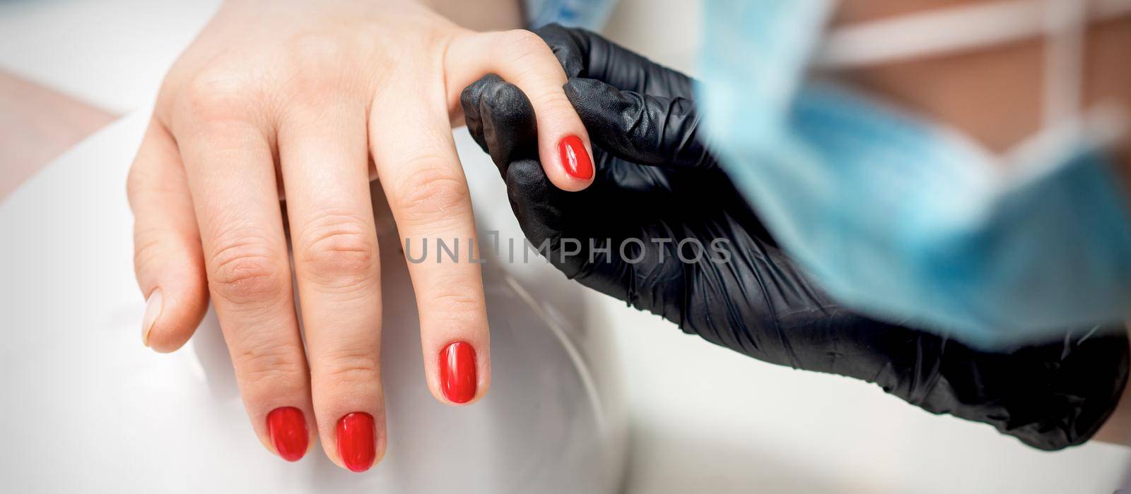 Young woman receives red nail polish by professional manicure master in nail salon