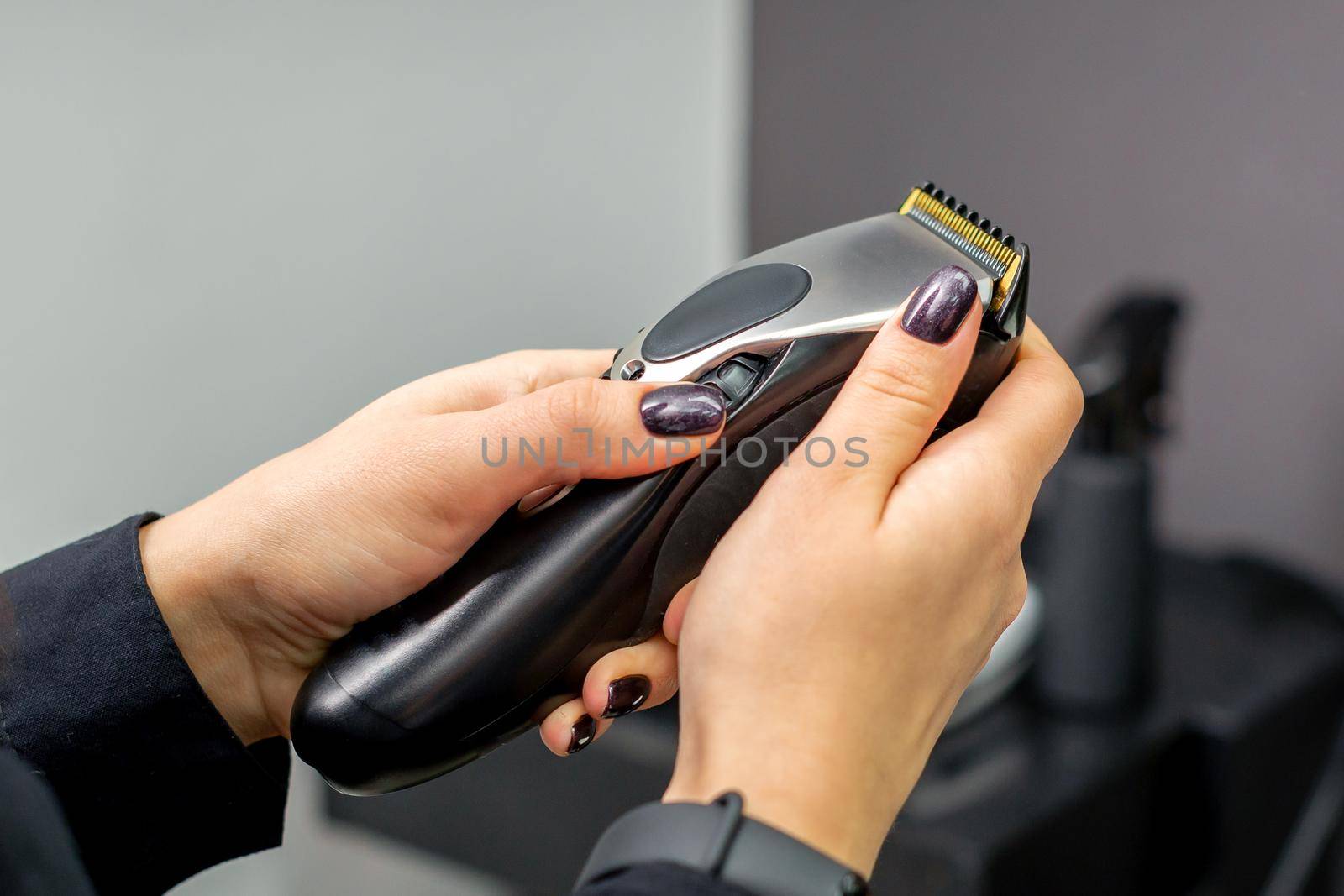 Hair clipper in hands of female professional hairdresser or barber in hair salon