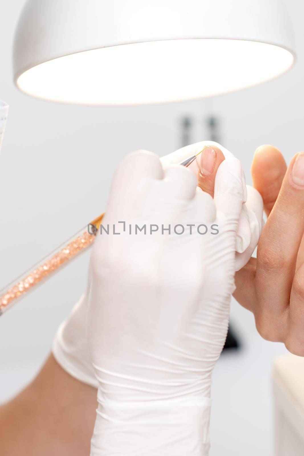 Professional manicure master drawing decorations by pink gel pencil on edge of a nail of young female