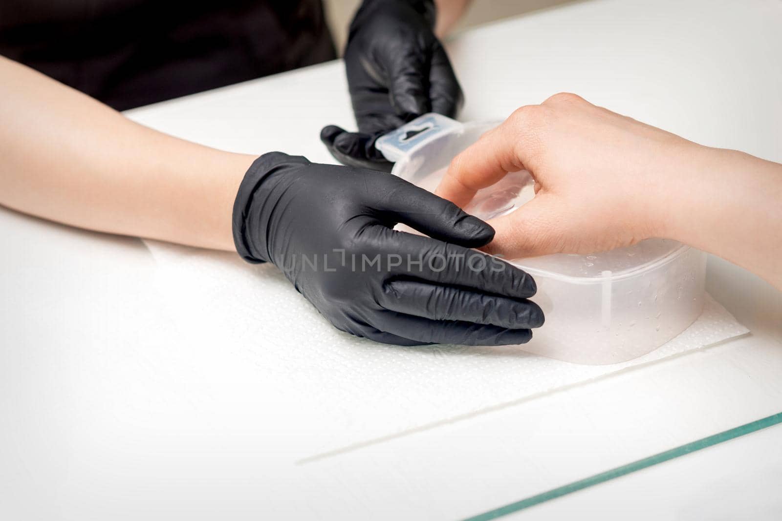 Soaking fingernails in the bath with water on white table under the supervision of a manicurist