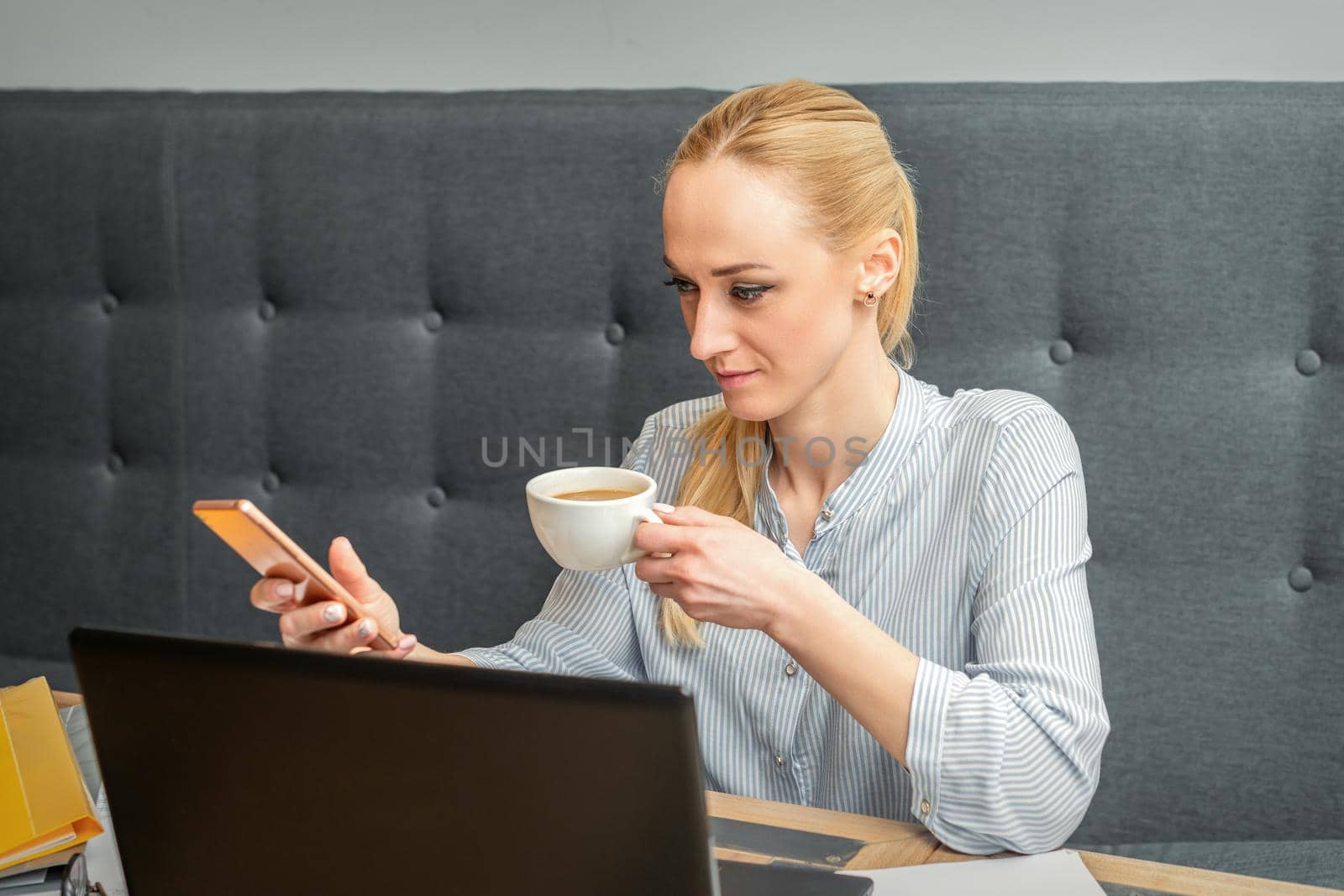 Young caucasian businesswoman with smartphone and cup of coffee working at home office