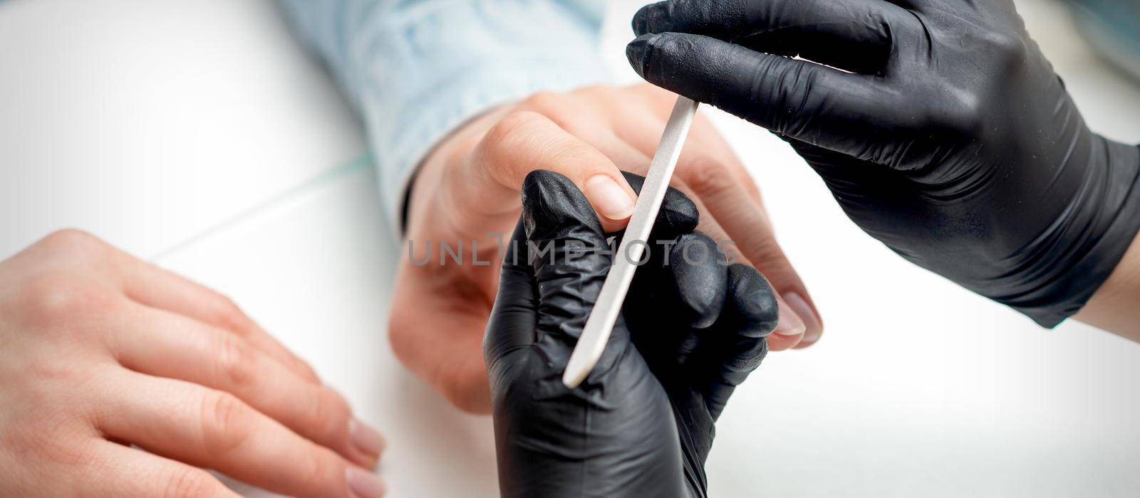 Closeup shot of young woman getting manicure by manicure master with nail file in nail salon