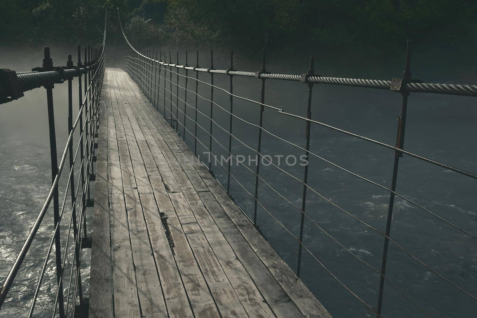 old wooden long suspension bridge over the Belaya mountain river, in nature, thick mystical fog over the water at night in the moonlight