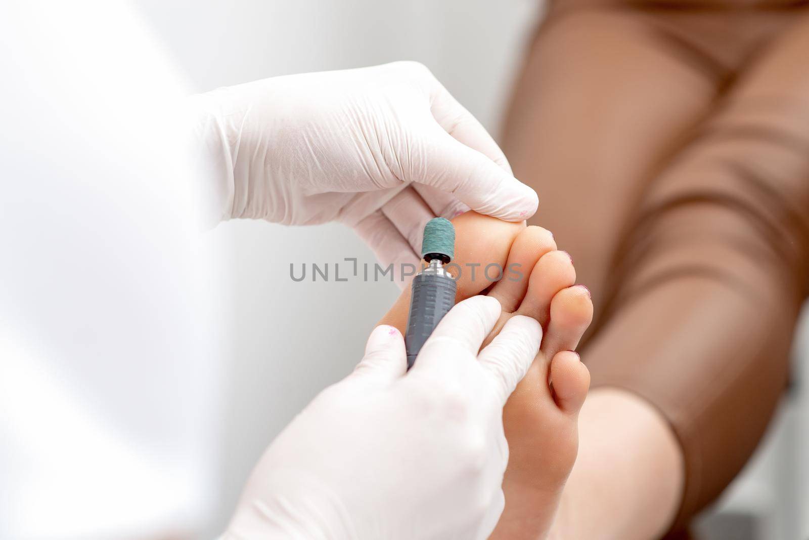 Peeling feet pedicure procedure from callus on foot by hands of podiatrist in white gloves at beauty salon