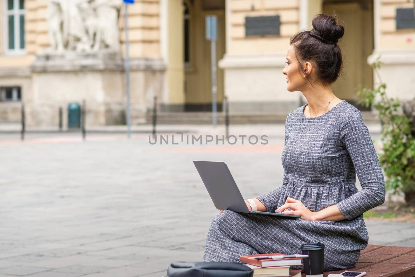 Student young woman uses laptop on the bench on the city street near university