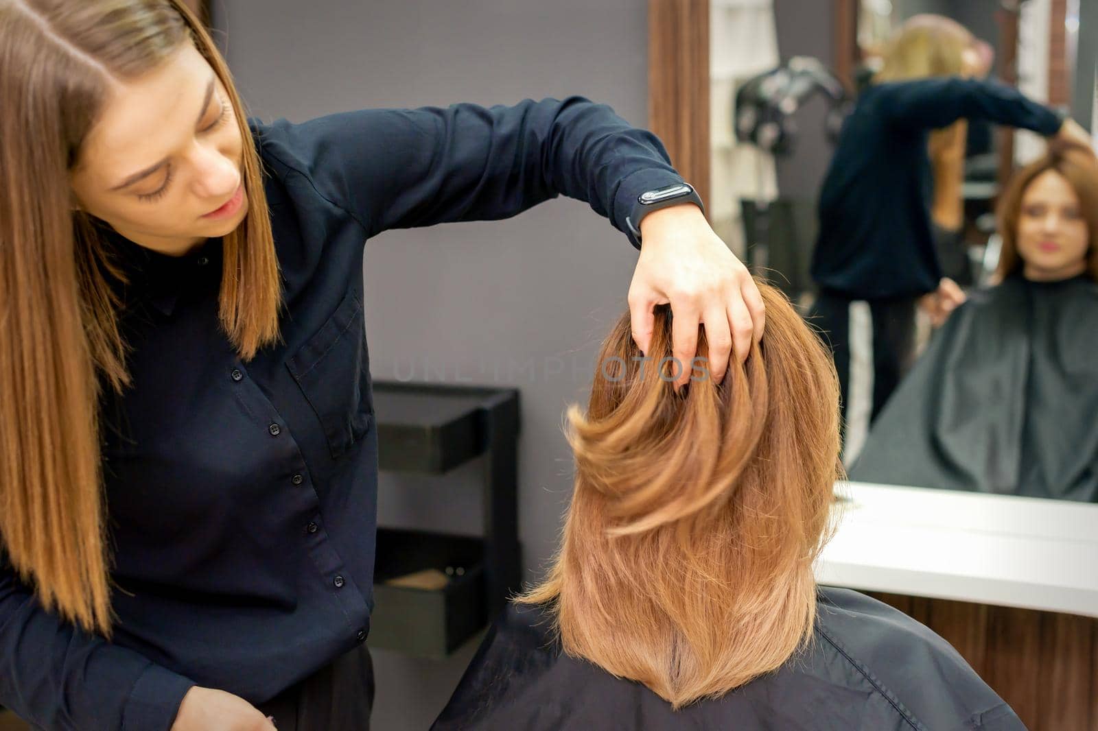 Back view of hairdresser checks red or brown hairstyle of young woman in hair salon