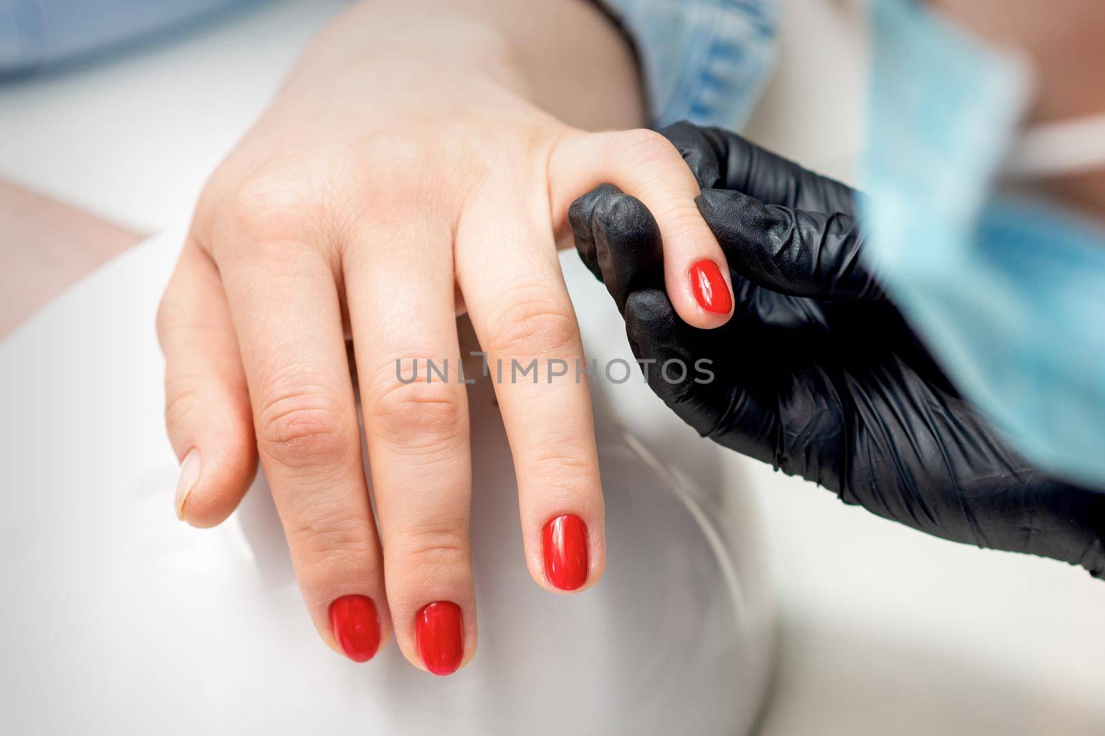 Young woman receives red nail polish by professional manicure master in nail salon