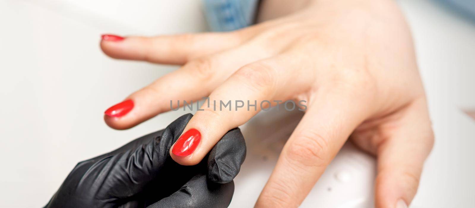 Young woman receives red nail polish by professional manicure master in nail salon