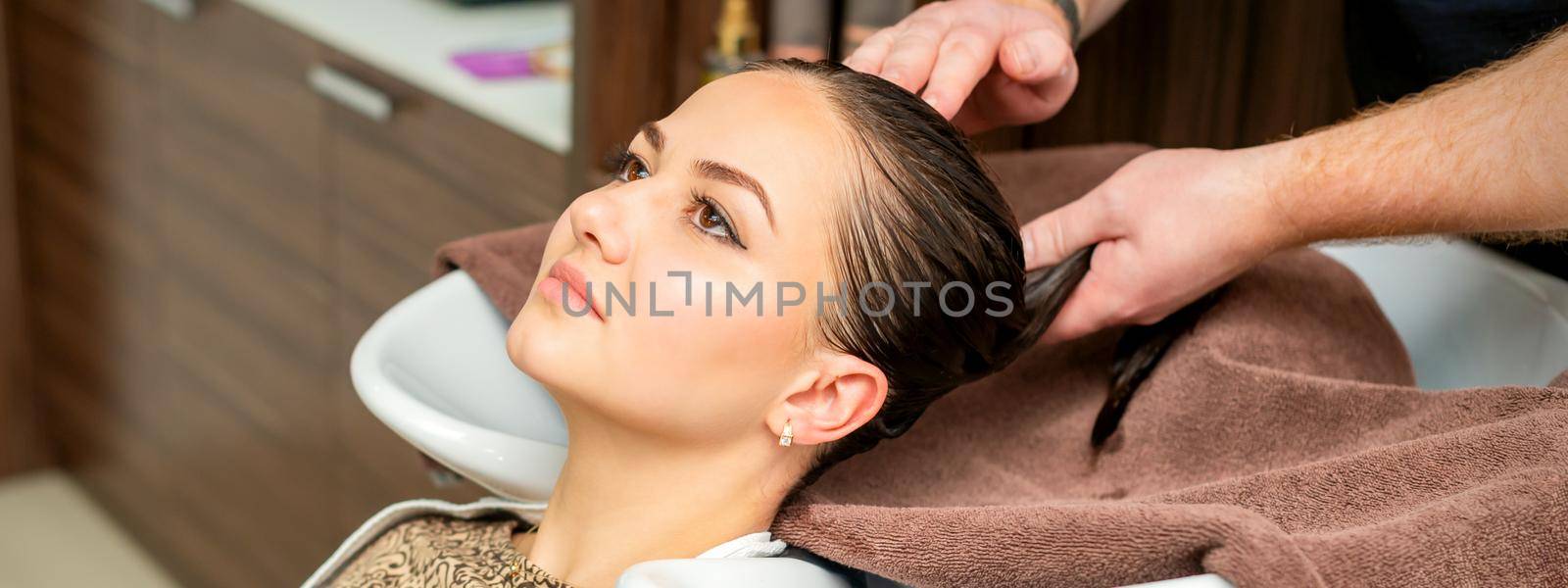 Hairdresser wipes the hair with towel of young woman after shampooing in hair salon