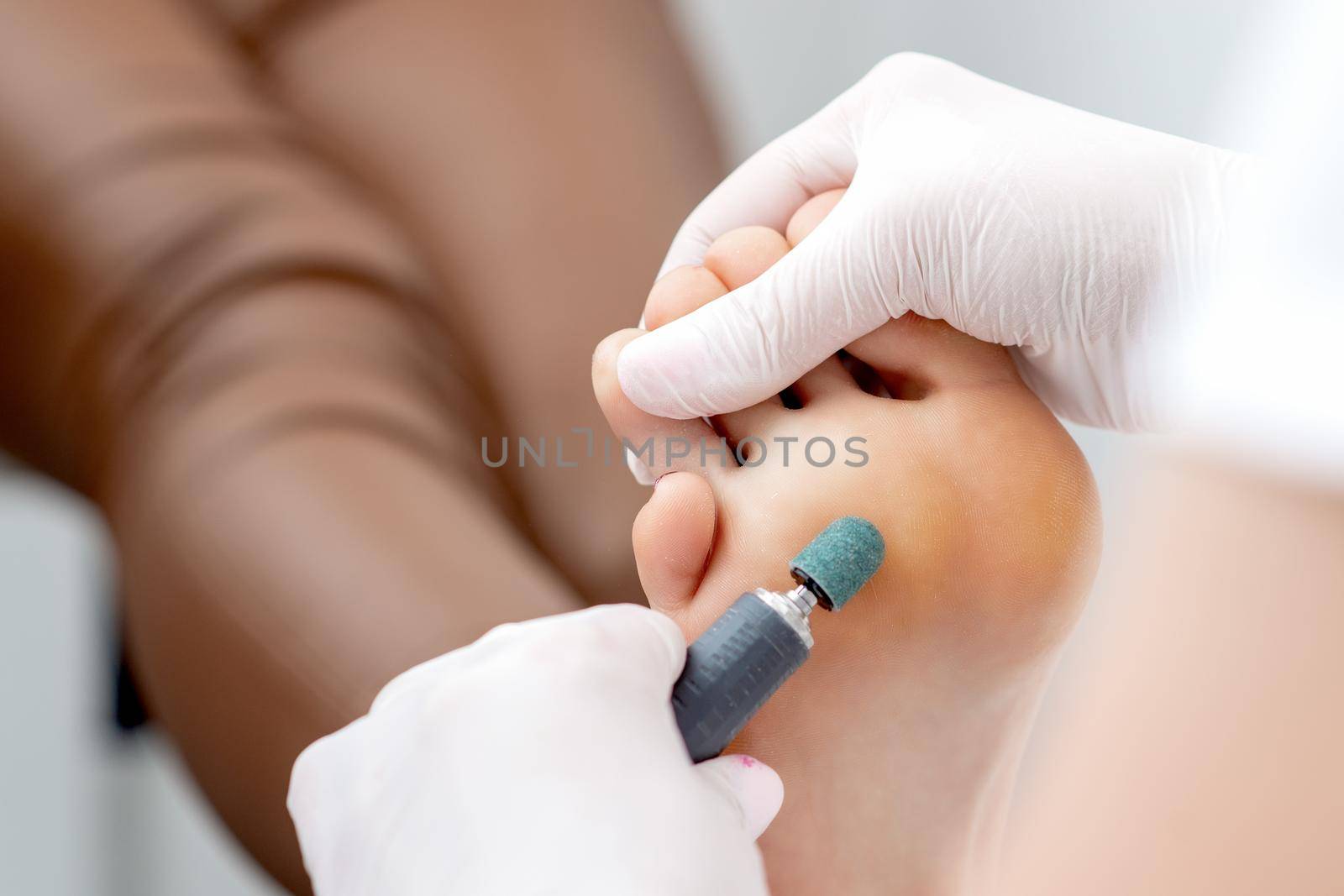 Peeling feet pedicure procedure from callus on foot by hands of podiatrist in white gloves at beauty salon