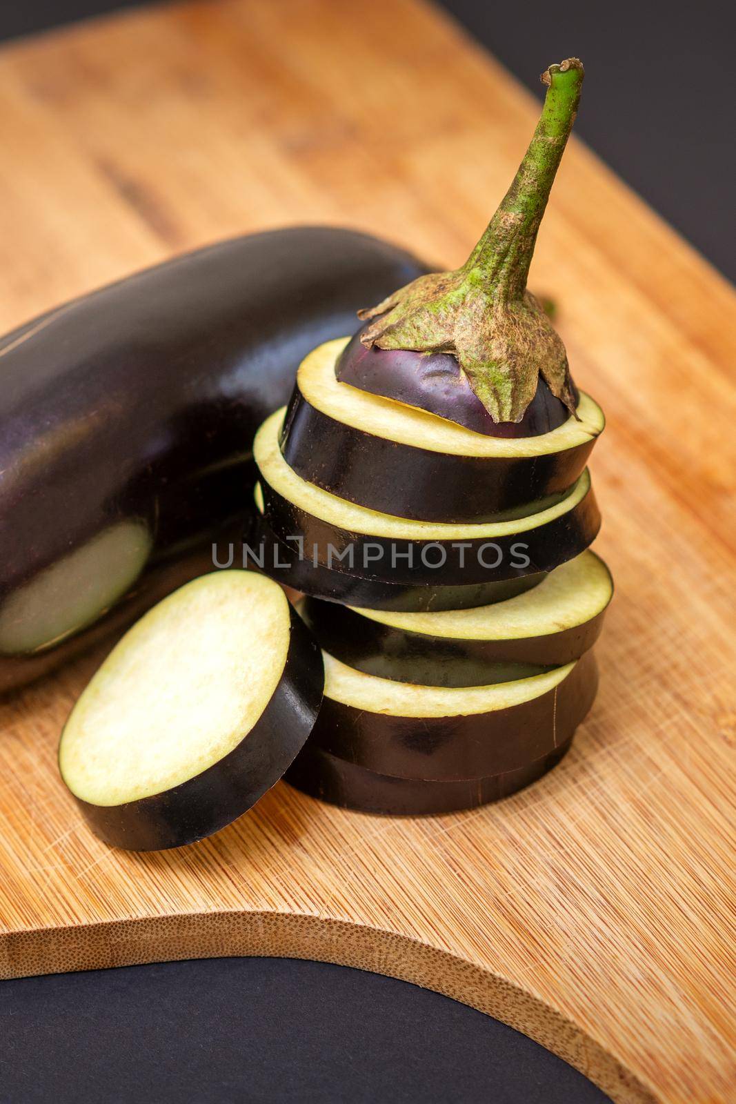 Fresh sliced eggplant on wooden cutting board isolated on black. Cooking ingredients