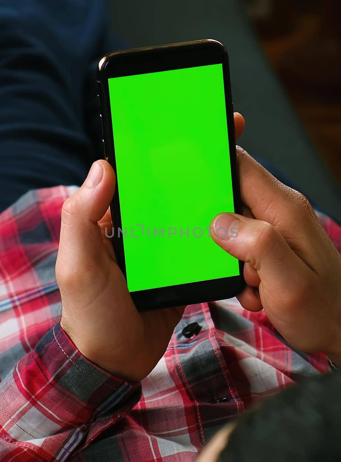 A man holds a phone in his hands with a green screen. Selective focus. People.