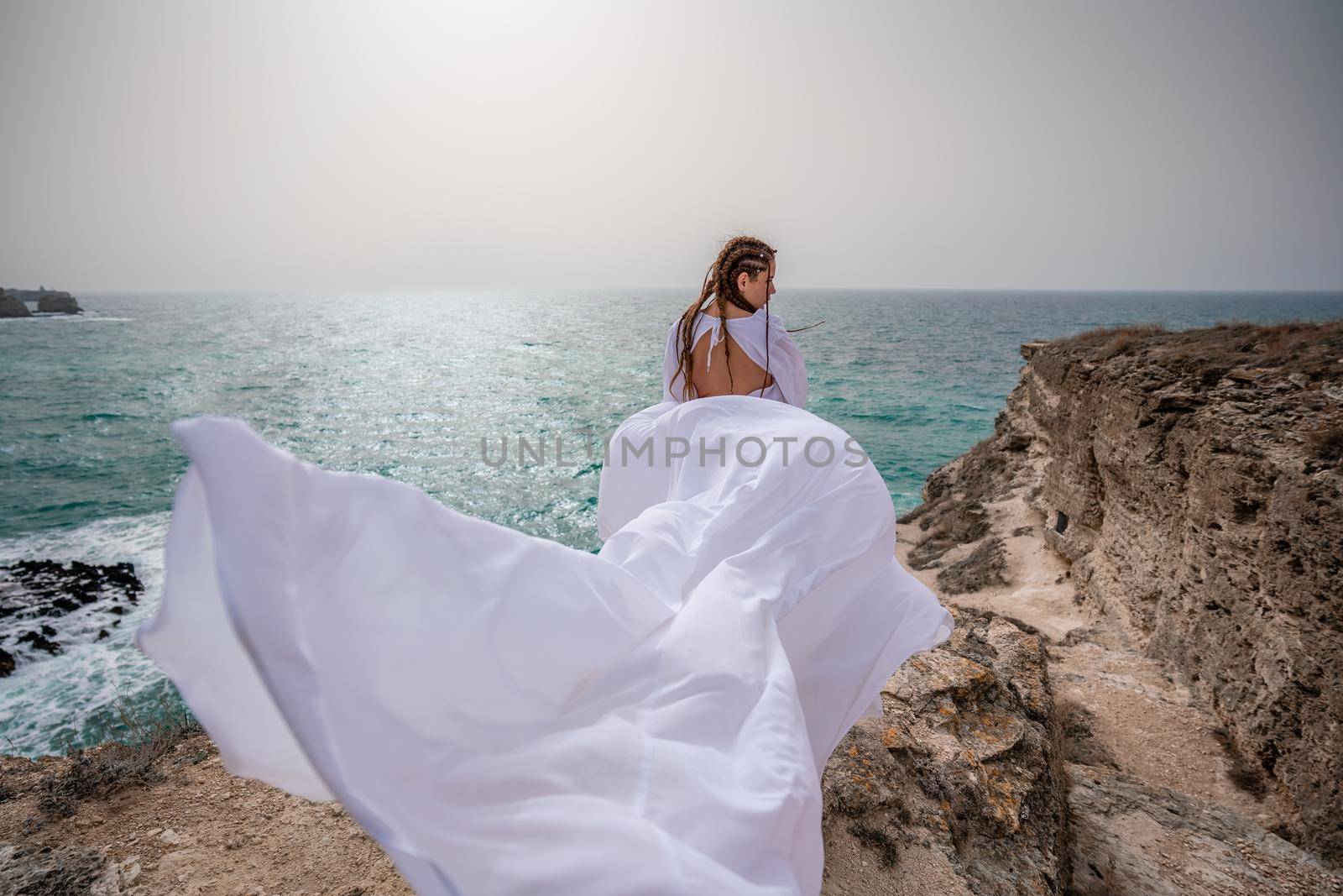 Happy freedom woman on the beach enjoying and posing in white dress. Rear view of a girl in a fluttering white dress in the wind. Holidays, holidays at sea