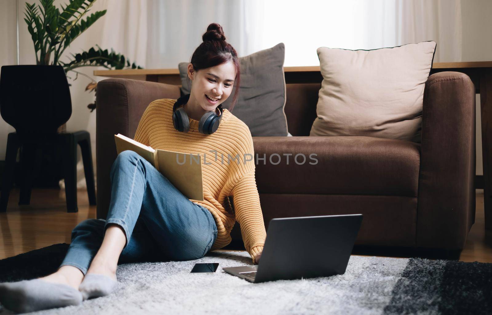 Young asian women listening to music in headphones Attractive Asian girl looking at the laptop sitting in the living room spending leisure time at home by wichayada