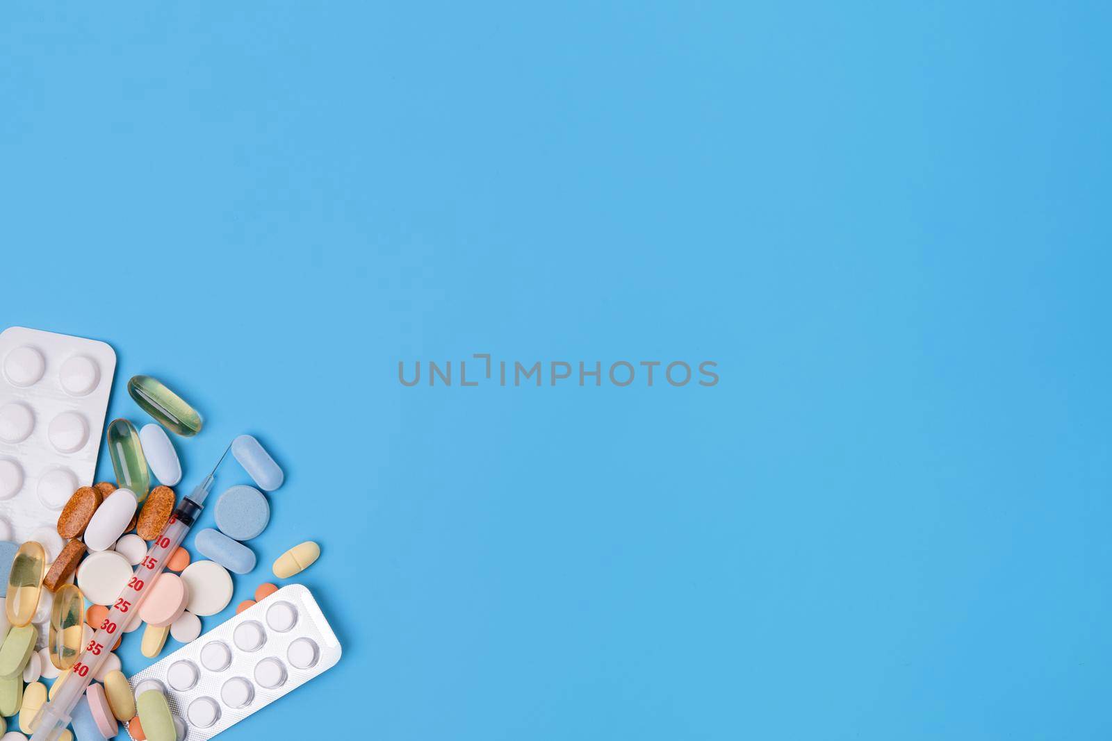 Pills, vitamins and disposable syringe, heart, stethoscope on blue background top view Space for text. see doctor.